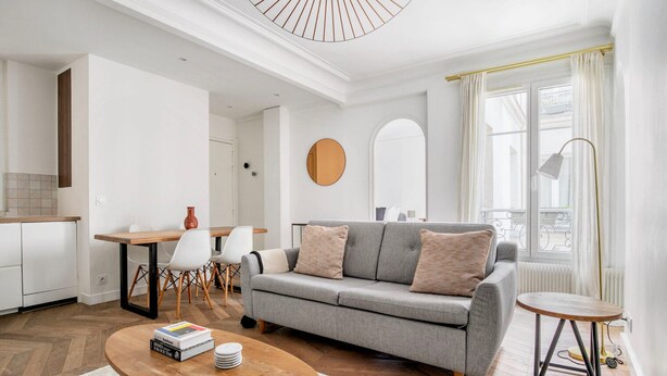 Ein modernes Wohnzimmer mit einer grauen Couch, einem Holztisch und einem Essbereich mit einem Holztisch und weißen Stühlen.