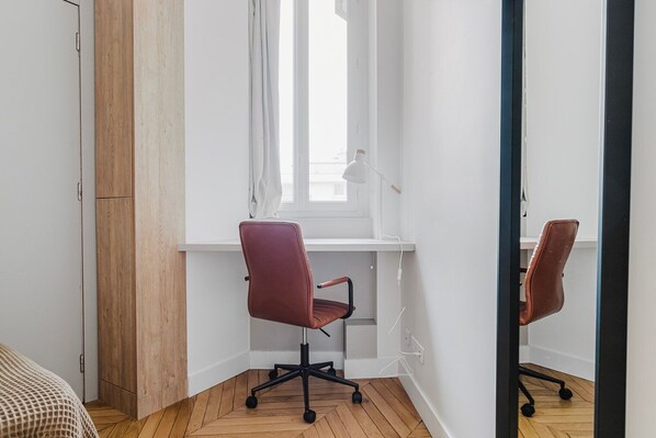 A modern office space with a wooden desk, a swivel office chair, and a large mirror reflecting the room.