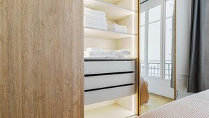 Ein Schlafzimmer mit einem hölzernen Kleiderschrank, einem Bett mit gemustertem Überwurf und Blick auf einen Balkon durch ein Fenster.