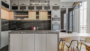 Eine moderne Küche mit Marmor-Spritzschutz, eingebauten Geräten und einem Essbereich mit Holztisch und -stühlen.