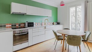 Eine moderne Küche mit grüner Wand, weißen Schränken, einem eingebauten Backofen und einem Essbereich mit rundem Tisch und Stühlen.