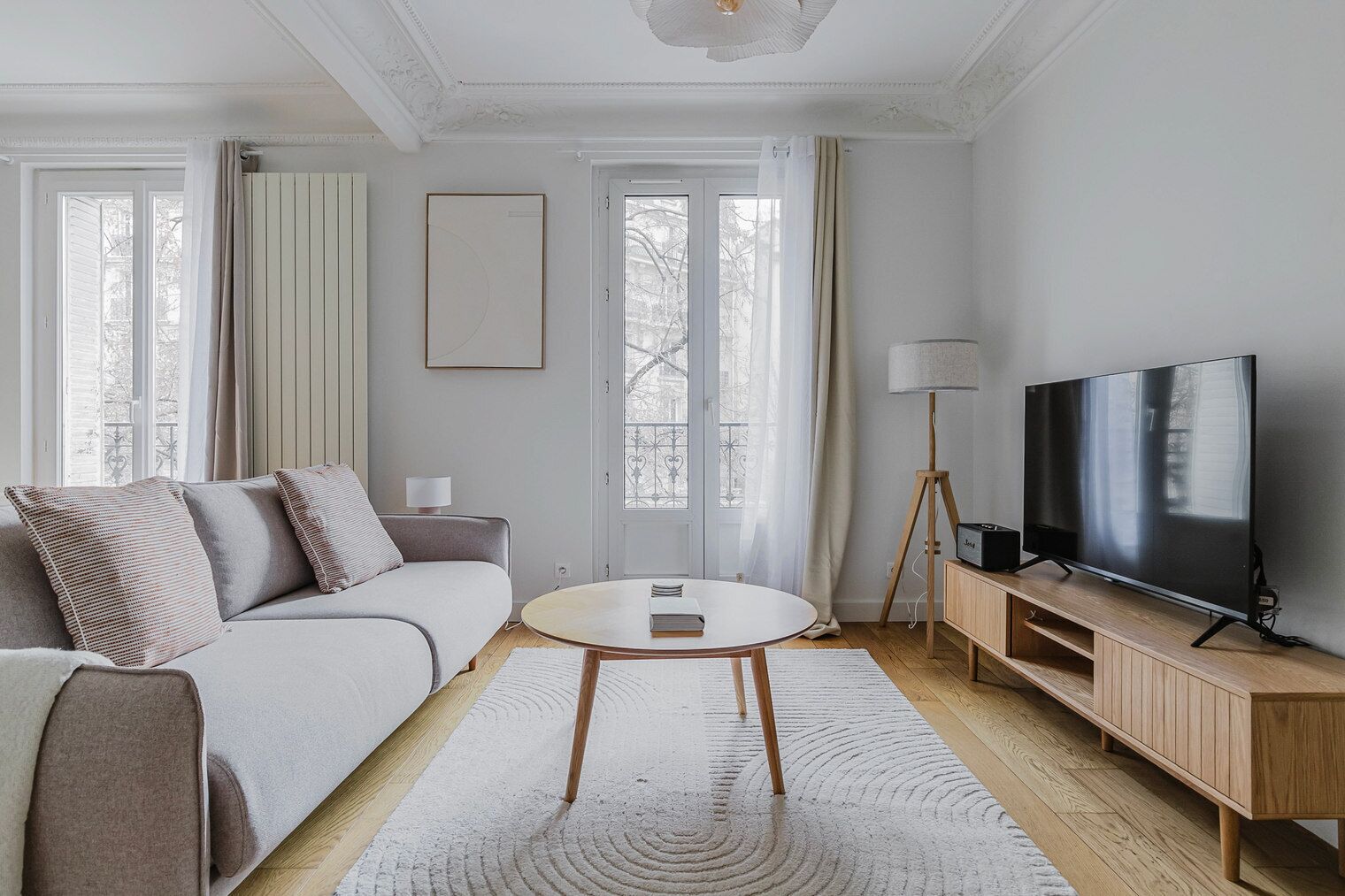 A modern living room with a sofa, a round coffee table, a TV on a wooden stand, and a floor lamp.