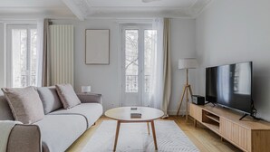Ein modernes Wohnzimmer mit einer Couch, einem runden Couchtisch, einem Fernseher auf einem Holzgestell und einer Stehlampe.