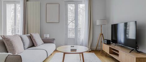 A modern living room with a sofa, a round coffee table, a TV on a wooden stand, and a floor lamp.