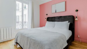 Ein Schlafzimmer mit Bett, rosafarbenen Wänden, einem Fenster und einer Heizung.
