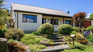 A house with a sloped roof, a front porch, and a well-maintained garden with various plants and a mailbox. - Criffel Peak Cottage, quiet location, only 10 min walk into Wanaka town centre (Wānaka)