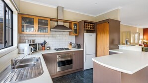 A modern kitchen with a central island, stainless steel appliances, and wooden cabinetry. - Criffel Peak Cottage, quiet location, only 10 min walk into Wanaka town centre (Wānaka)
