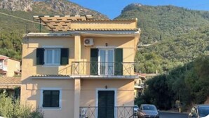 A two-story building with a balcony and a mountain in the background. - Nissaki Rooftop Oceanview two bedroom apartment with WiFi and air conditioning (Nisaki)