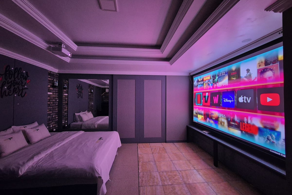 Un dormitorio moderno con una televisión de pantalla plana grande que muestra diversos servicios de transmisión.