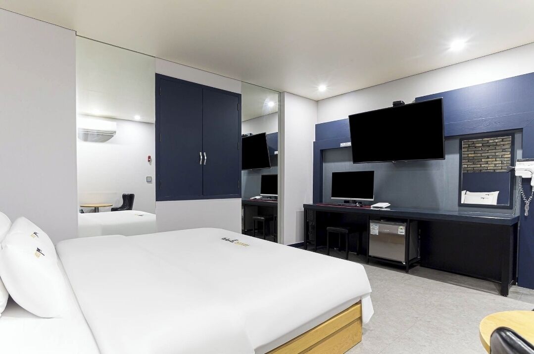 A modern hotel room with a large bed, a desk with a computer, and a flat-screen TV mounted on the wall.