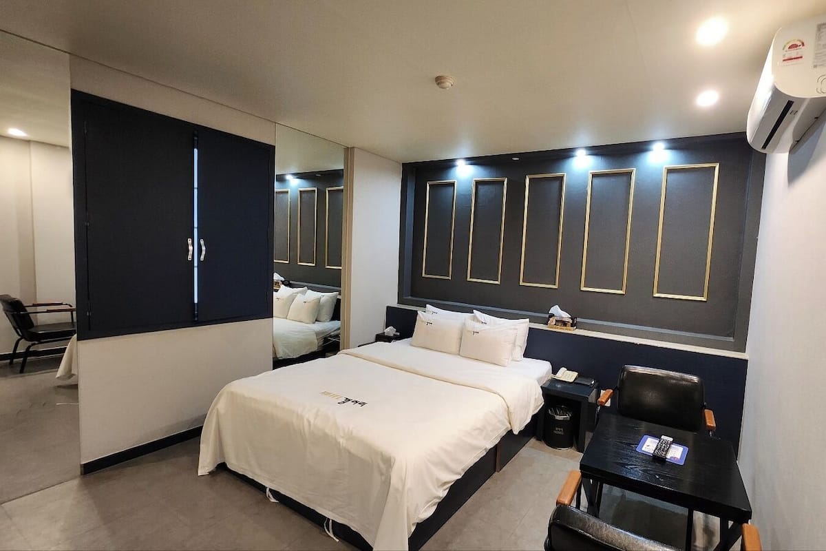 Una habitación de hotel con cama, mesita de noche, una silla y un escritorio con otra silla.