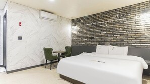 A hotel room with a bed, a small table, two chairs, a marble wall, a brick wall with a motivational quote, and an air conditioning unit. - Pyeongtaek Station Gallery Hotel (Pyeongtaek)