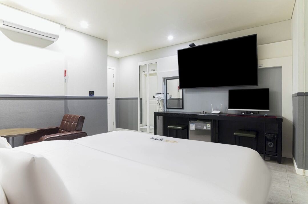 A hotel room with a large bed, a desk with a flat-screen TV, a chair, and a small table.