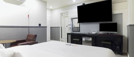 A hotel room with a large bed, a desk with a flat-screen TV, a chair, and a small table.