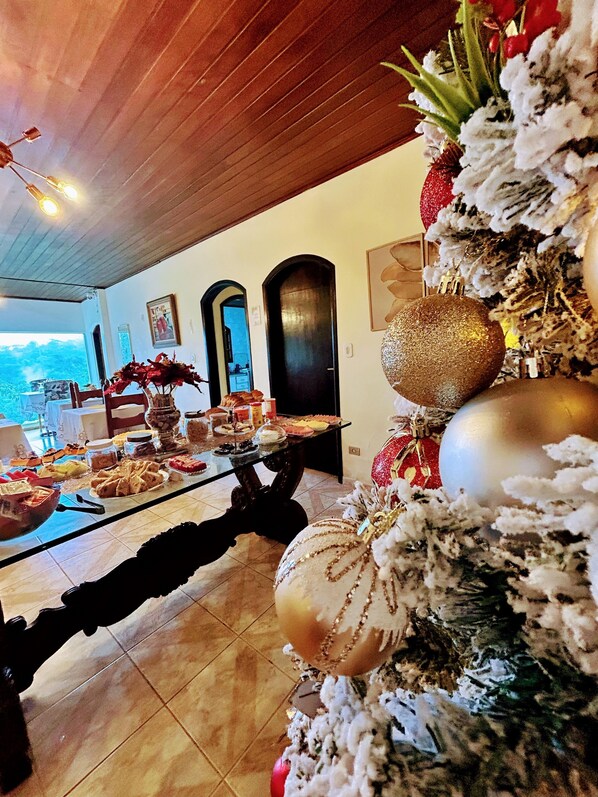 Un comedor con un árbol de Navidad, una mesa de cristal con comida y vistas al exterior.