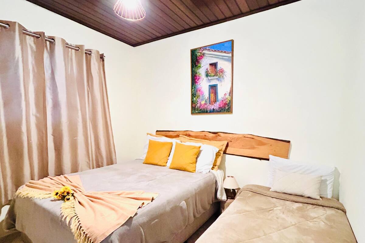 A bedroom with a bed, a bedside table, a lamp, a painting on the wall, and a window with curtains.