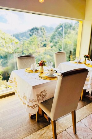 A dining table set for four with a view of a mountainous landscape through large windows. - Pousada Valle do Sol (Campos do Jordão)