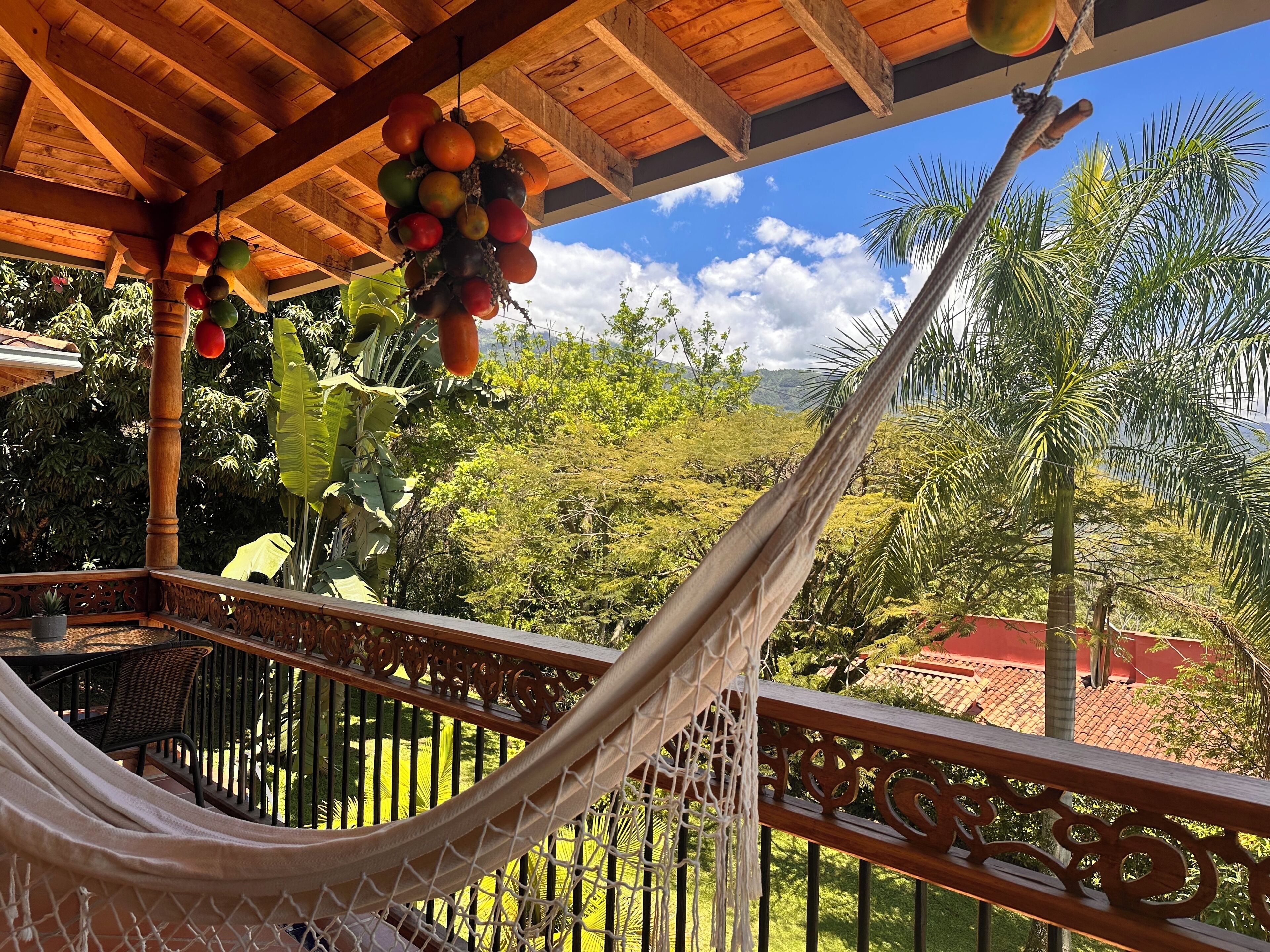 A hammock on a balcony with a view of lush greenery and a wooden ceiling.