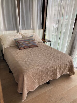 Ein ordentlich bezogenes Bett mit einer beigen Tagesdecke, zwei Kissen und einem Nachttisch mit einer Lampe.