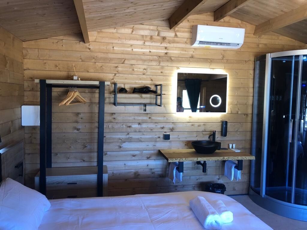 Una habitación de cabaña de madera con una cama, un lavamanos pequeño, un espejo y una puerta corredera.