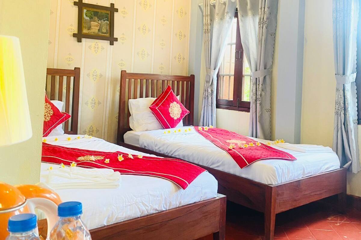 A hotel room with two wooden beds, a wooden ceiling, and a window with curtains.