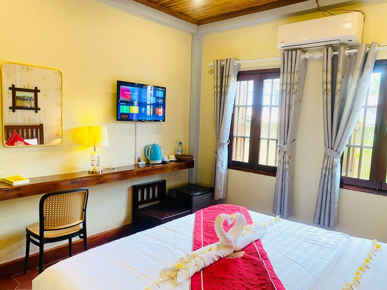 A hotel room with a bed, a desk with a lamp, a television, and a window with curtains.