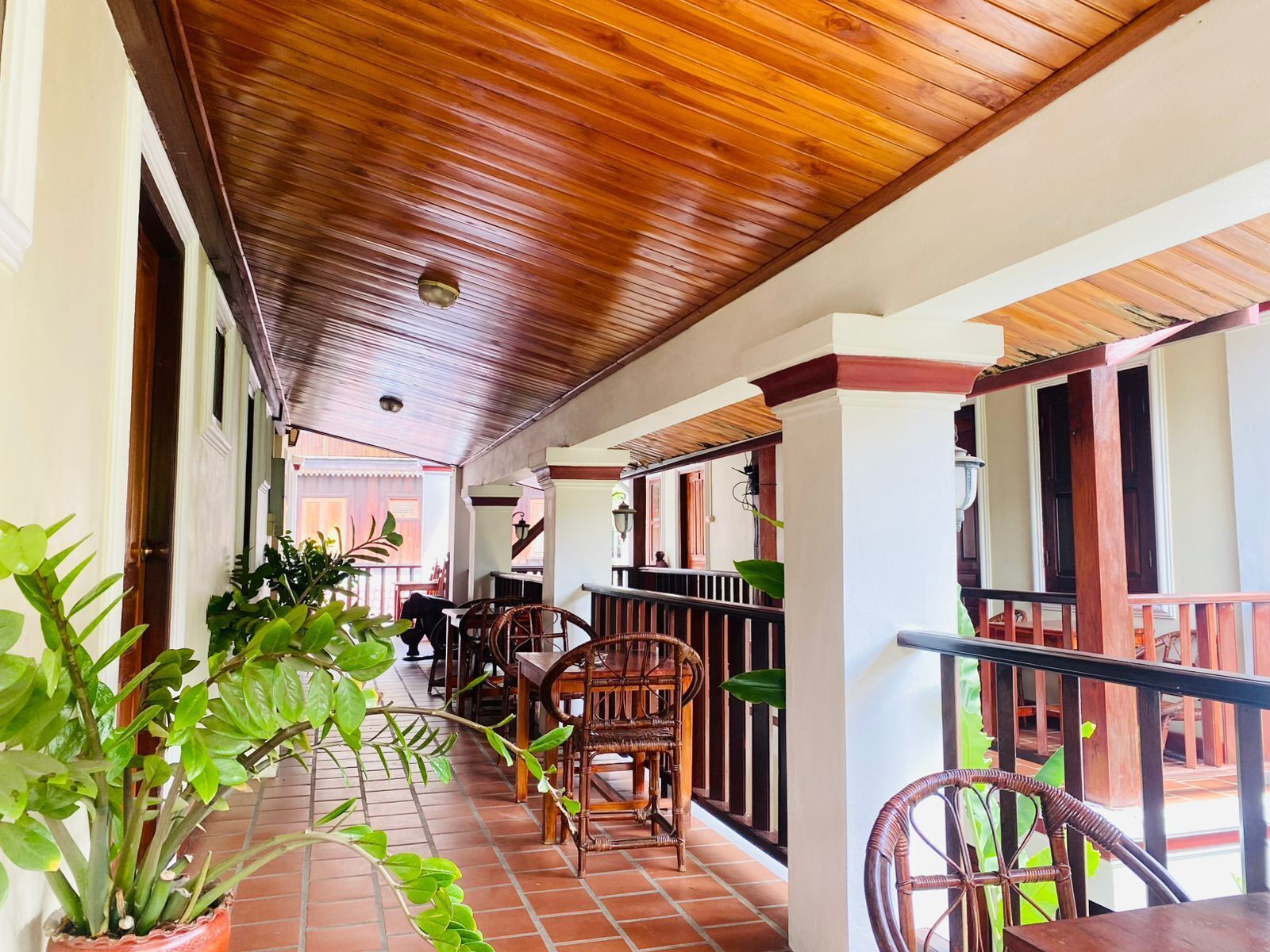 A covered outdoor area with wooden flooring, wicker furniture, and potted plants.