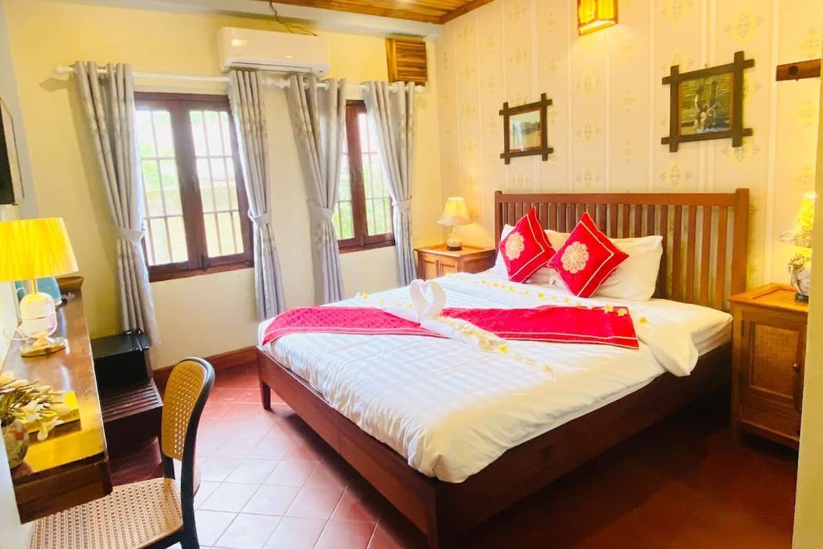 A neatly arranged bedroom with a wooden bed, a desk with a lamp, and a chair.