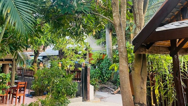 Un espace extérieur de style tropical, avec une table en bois, des chaises et un banc en pierre.