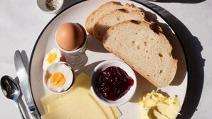 Une assiette de petit-déjeuner avec du pain, des œufs, du fromage, du beurre et de la confiture.