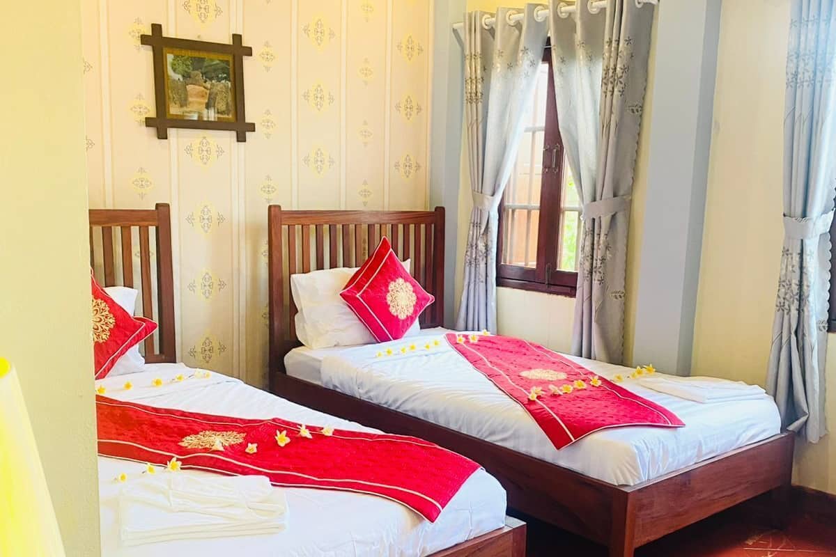 A room with two wooden beds, a wooden ceiling, and a window with curtains.