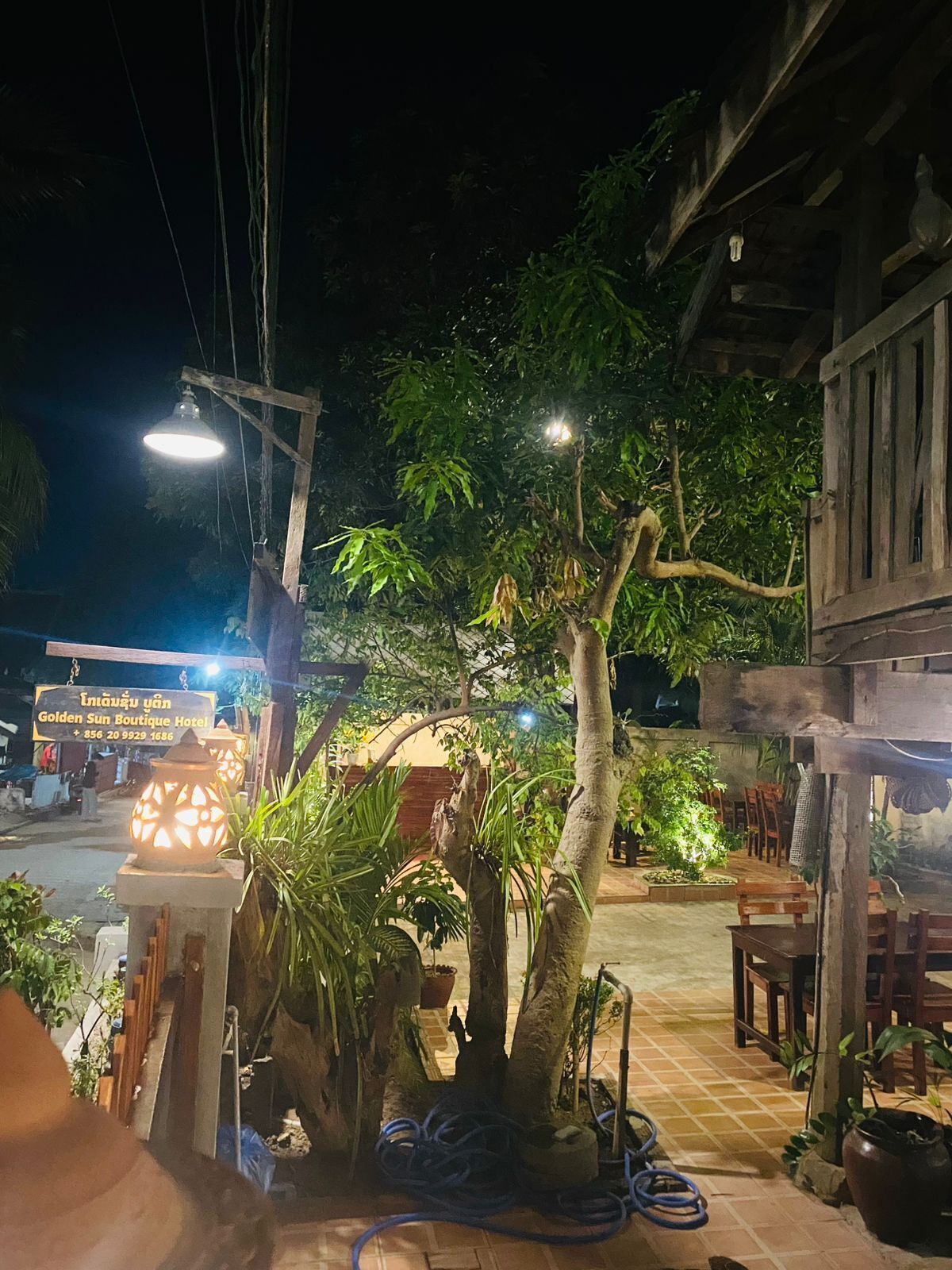 Una vista nocturna de un hotel con un letrero, mesas al aire libre y un jardín bien iluminado.