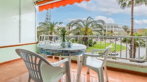Un balcon avec une table ronde et des chaises, une vue sur des palmiers et un bâtiment en arrière-plan.