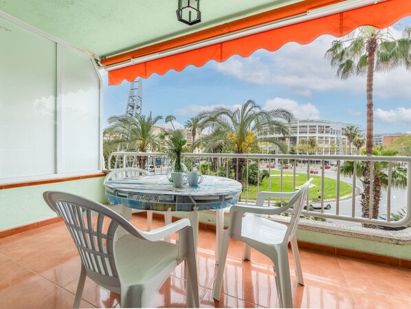 A balcony with a round table and chairs, a view of palm trees and a building in the background.