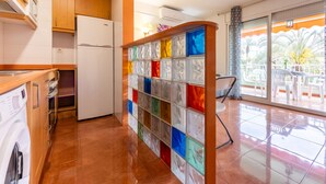 Une cuisine moderne avec des meubles en bois, un réfrigérateur blanc et une cloison en verre aux couleurs vives.