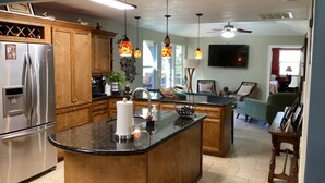 Una cocina con armarios de madera, un refrigerador de acero inoxidable, una isla central, luces colgantes y un ventilador de techo.