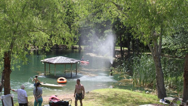 Un entorno junto al río con un pabellón, una canoa y personas cerca del agua.