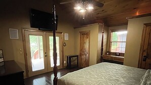 Un dormitorio con cama con dosel, piso de madera, ventilador de techo y televisión en la pared.
