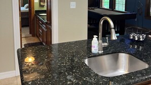 Una cocina con encimeras de granito, un lavamanos de acero inoxidable y luces colgantes.
