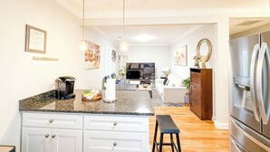 Uma cozinha moderna com bancadas de granito, armários brancos, geladeira de aço inoxidável e uma ilha central com banquetas.
