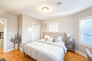 A bedroom with a large bed, a bedside table with a lamp, a window with blinds, and a door leading to another room. - 40-Newly renovated, stylish and beautiful apt/4br close to Highway (Boston)