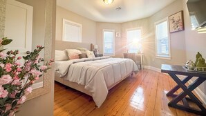 Quarto com cama, mesas de cabeceira, cómoda e janela com persianas.