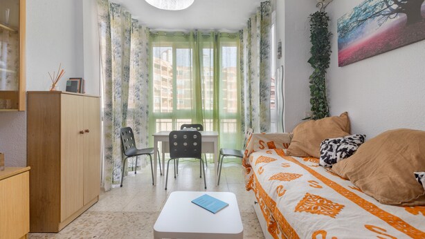Un dormitorio con cama, escritorio, sillas, armario y ventana con cortinas.