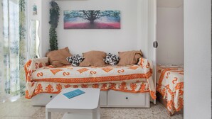 Una habitación con una cama, una mesita, aire acondicionado de pared y un cuadro de un árbol.