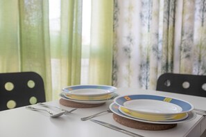 A dining table with plates, cutlery, and glasses, set against a backdrop of curtains.