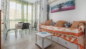 Una sala de estar con sofá, una mesita, una silla, una mesa de comedor y un ventanal con cortinas.
