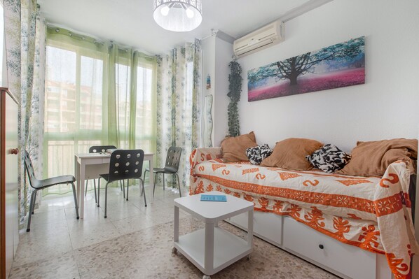 A living room with a sofa, a small table, a chair, a dining table, and a window with curtains.