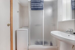 A bathroom with a glass shower enclosure, a white sink, and a towel hanging on the shower door.