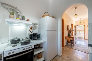 A compact kitchen with a stove, pots, a refrigerator, and a dining area with a chair and table.