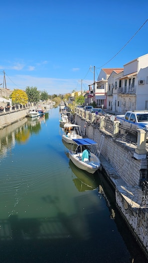 A canal with boats docked along the side, a stone wall, and buildings with balconies.